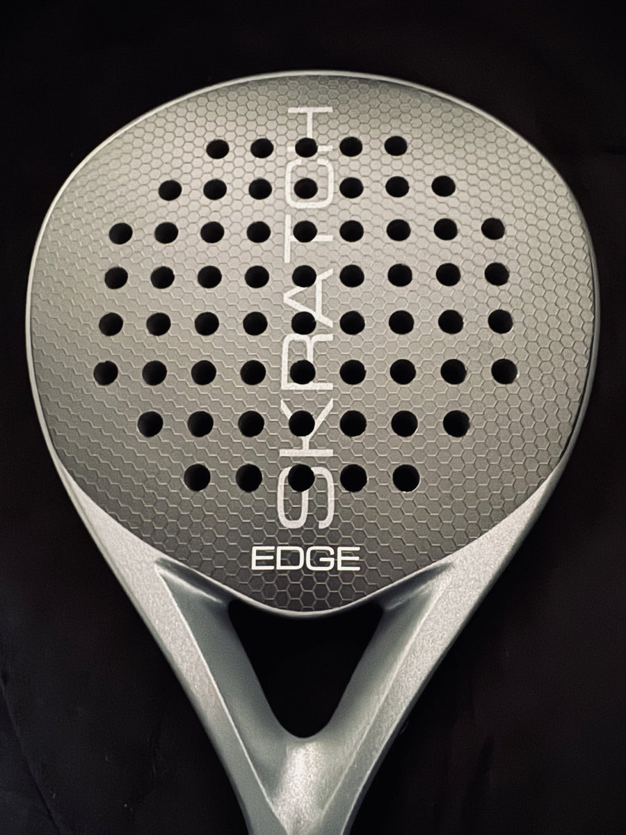 SKRATCH EDGE padel racket face-on on black, matte black 12K carbon face with hex-spin texture and charcoal grey pearlescent frame.